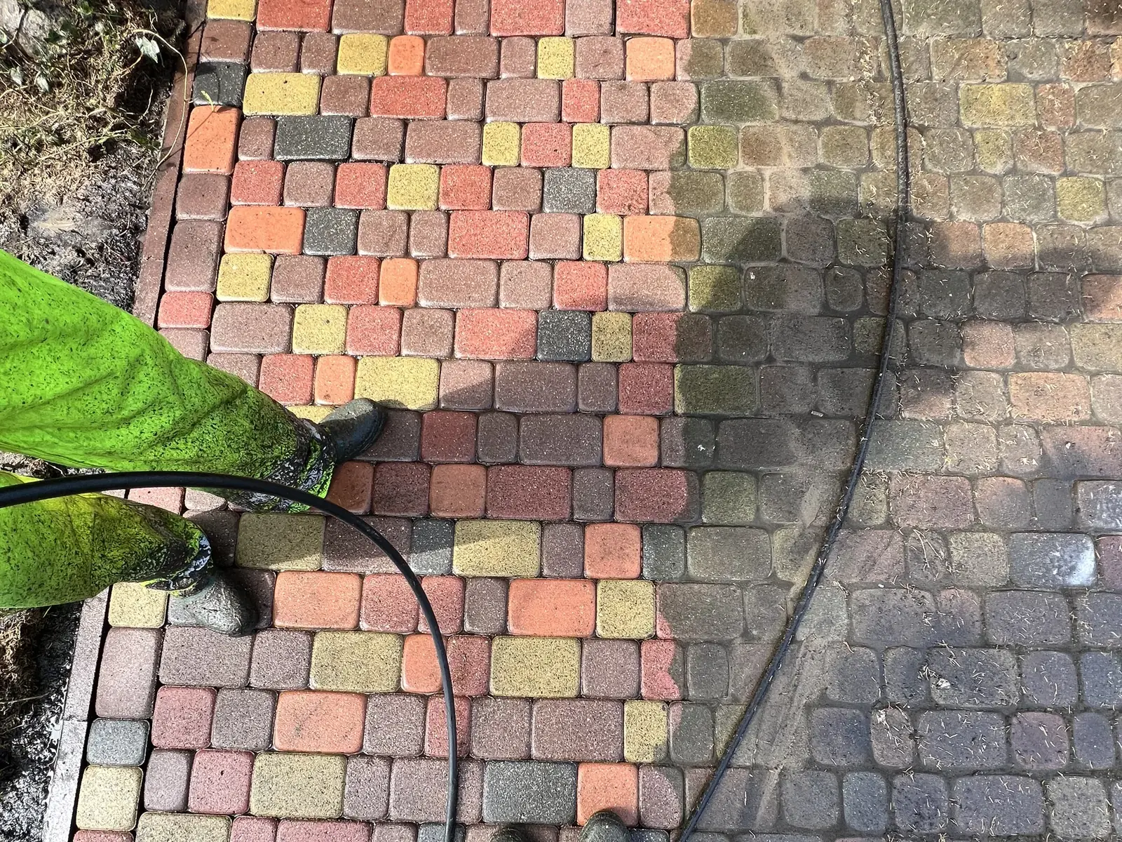 Mycie ciśnieniowe kolorowej kostki brukowej, widoczna wyraźna granica między czystą a zabrudzoną powierzchnią