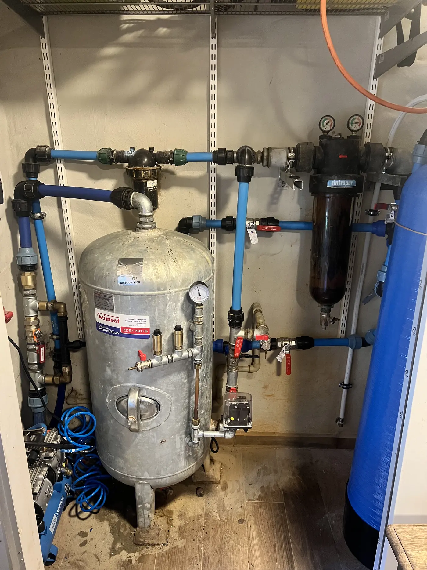 Zbiornik hydroforowy, filtry i niebieskie rury wodne w pomieszczeniu technicznym po modernizacji