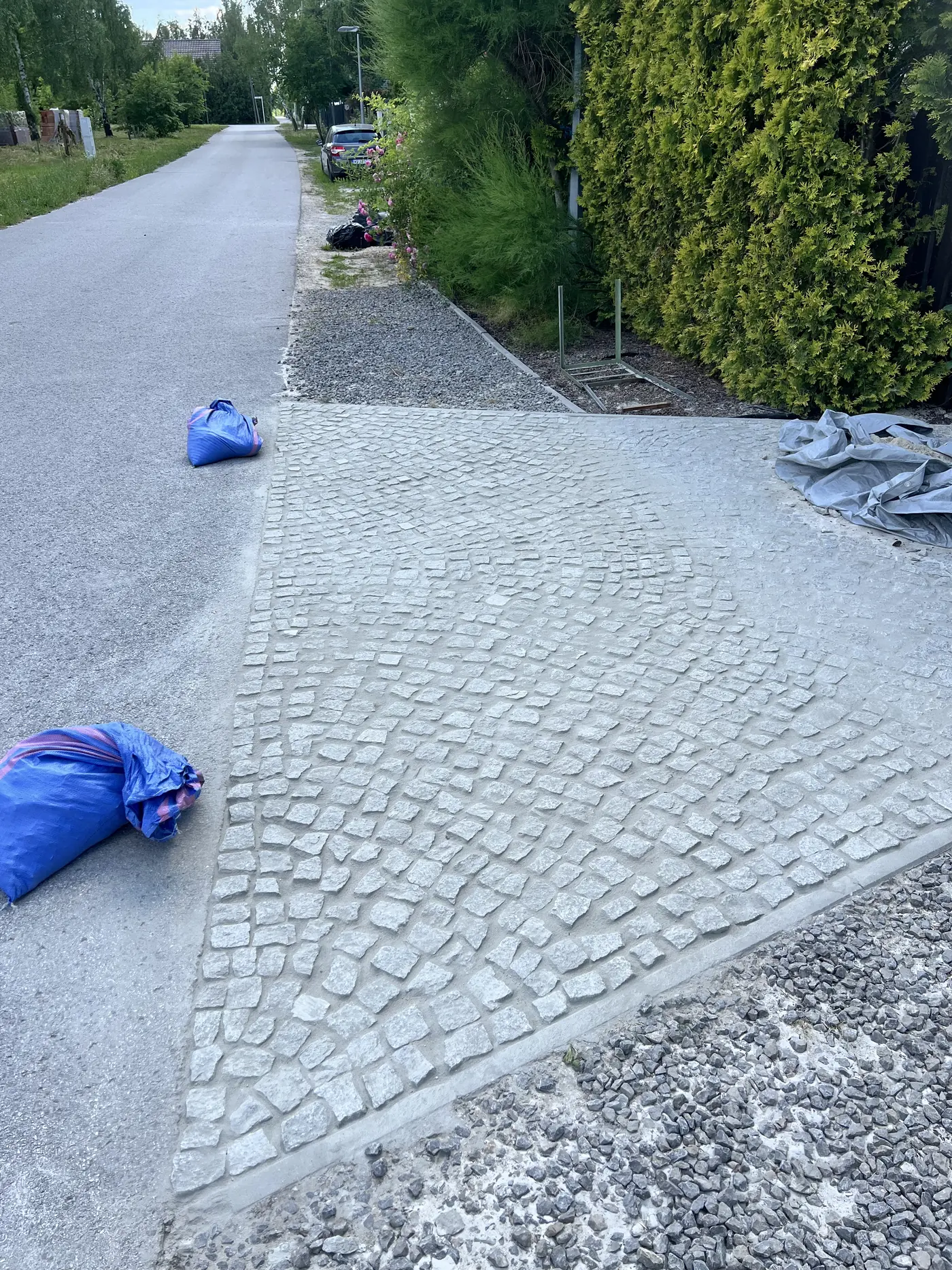 Świeżo ułożony wjazd z jasnej kostki granitowej z zasypanymi fugami, przy krawędzi worki z materiałem